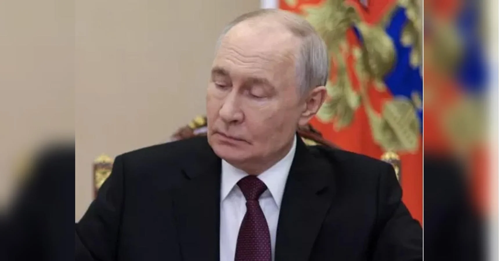 Володимир Путін у костюмі сидить на тлі російського державного прапора