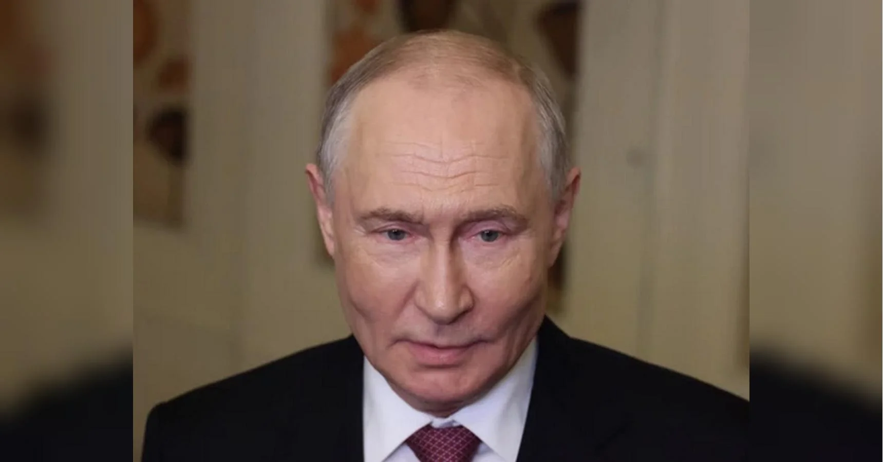 Володимир Путін у чорному костюмі з бордовою краваткою дивиться вниз
