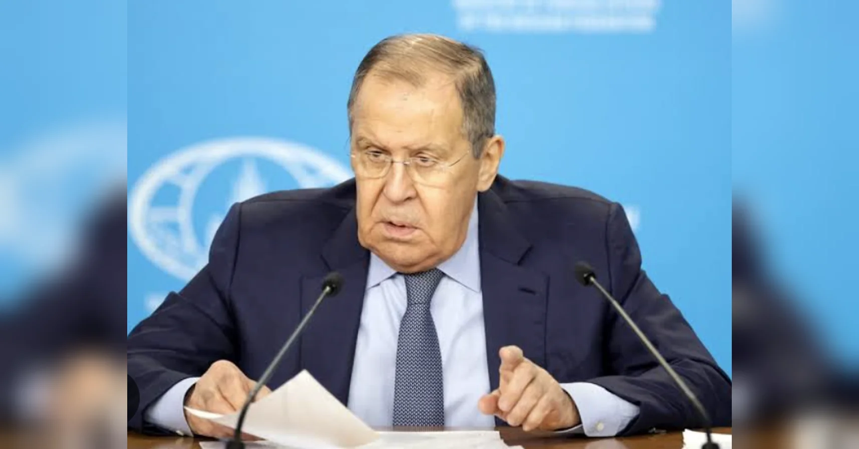 Чоловік у темному костюмі та окулярах говорить на прес-конференції біля мікрофонів