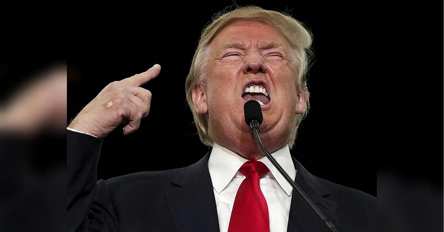 Дональд Трамп виступає в мікрофон і вказує пальцем на темному тлі