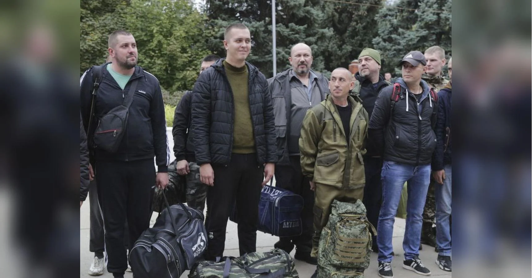Чоловіки з дорожніми сумками стоять на тротуарі біля дерев
